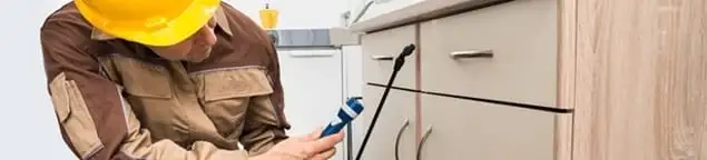 Roach exterminator applying treatment under kitchen cabinets in Naperville, IL